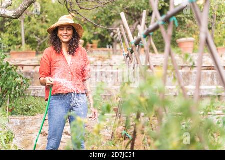 Belle femme souriante arroser les plantes depuis le tuyau au jardin Banque D'Images