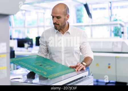 Un technicien homme expérimenté et fiable examine une grande carte de circuit imprimé en usine Banque D'Images