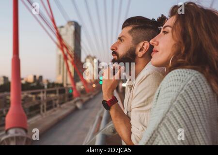 Couple attentionné qui regarde loin en se tenant sur le pont en ville Banque D'Images