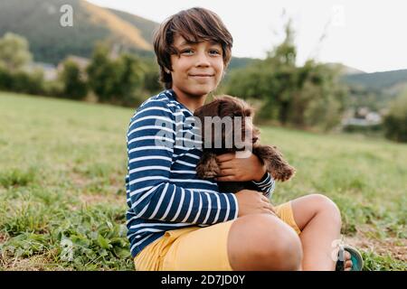 Garçon tenant le chiot tout en étant assis sur l'herbe à l'arrière-cour Banque D'Images