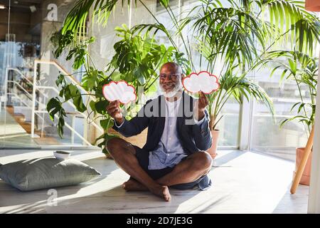Homme souriant tenant une bulle de pensée avec une jambe transversale assise à accueil Banque D'Images