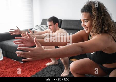 Couple accroupi tout en faisant de l'exercice ensemble à la maison Banque D'Images