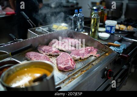 Cuisson de la viande au gaz pendant que le chef travaille en arrière-plan à cuisine commerciale Banque D'Images