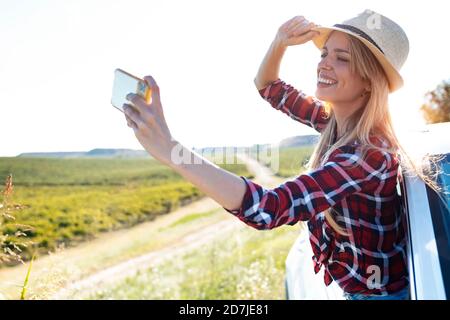 Une jeune femme prend son selfie par téléphone portable tout en se penchant de la fenêtre de voiture Banque D'Images