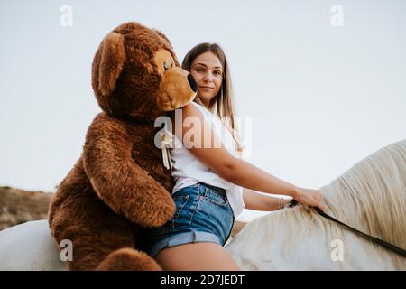 Portrait de la belle jeune femme à cheval avec grand teddy à porter derrière vous Banque D'Images