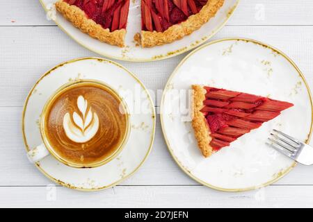 Rhubarbe maison et tarte aux fraises et une tasse de cappuccino au café sur une table en bois blanc. Vue de dessus. Banque D'Images