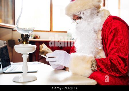 Homme portant le costume du Père Noël avec un ordinateur portable sur la table de lecture bible tout en étant assis à la maison Banque D'Images