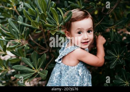 Jolie petite fille debout dans un parc public contre des feuilles vertes Banque D'Images