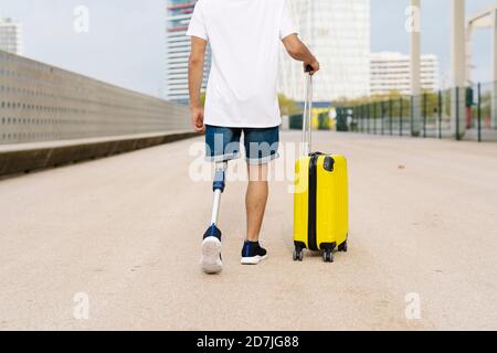 Jeune homme handicapé marchant avec des bagages sur le trottoir de la ville Banque D'Images