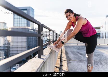Jeune femme souriante qui noue des lacets sur des rails contre le ciel Banque D'Images