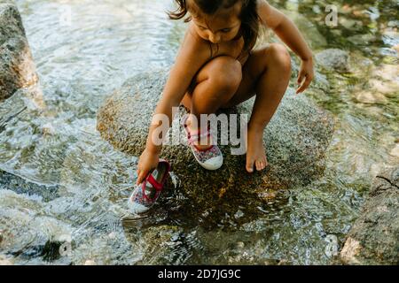 Jolie fille jouant dans l'eau courante tout en étant assise sur le rocher en été Banque D'Images