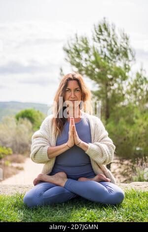 Femme faisant du yoga tout en étant assise sur l'herbe contre le ciel clair Banque D'Images