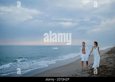 Jeune couple tenant la main tout en marchant sur la plage pendant le coucher du soleil Banque D'Images