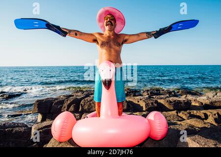 Homme gai portant un flipper de plongée à la main tout en étant debout anneau flamingo contre ciel clair Banque D'Images