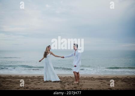 Couple tenant les mains tout en dansant contre la mer à la plage Banque D'Images