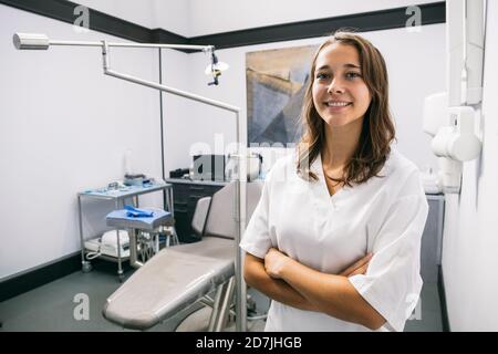 Jeune femme souriante assistante de dentiste debout avec les bras croisés clinique Banque D'Images