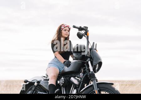 Jeune femme assise à moto contre le ciel Banque D'Images