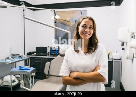 Femme souriante assistante de dentiste debout avec les bras croisés dans le bureau Banque D'Images