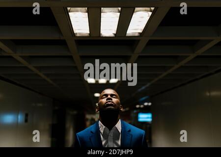Homme professionnel avec les yeux fermés debout sous la lumière éclairée métro Banque D'Images