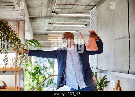 Homme mature tenant l'arrosage peut regarder la plante en se tenant debout à la maison Banque D'Images