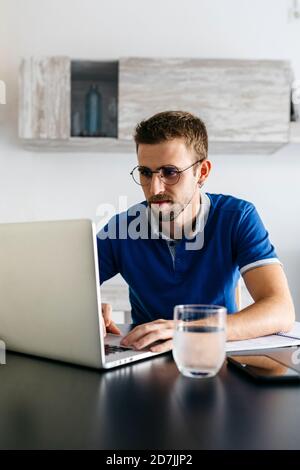 Jeune homme charmant utilisant un ordinateur portable tout en faisant des devoirs à table Banque D'Images