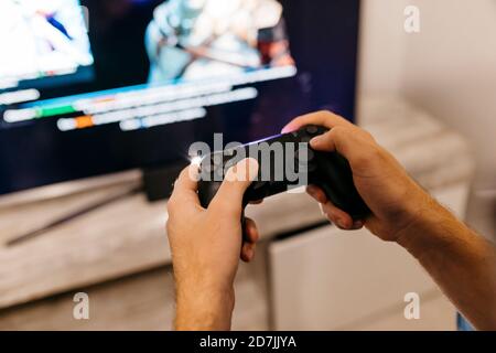 Mains d'un joueur masculin tenant la manette tout en jouant à la maison Banque D'Images