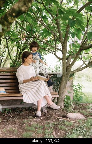 Belle femme et garçon lisant le livre tout en étant assis sur le banc à l'arrière-cour Banque D'Images