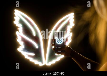 Bras de jeune femme prenant une photo de smartphone de blanc ailes au néon brillantes Banque D'Images