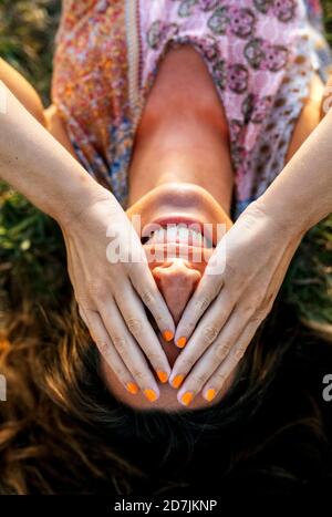 Jeune femme souriante couvrant les yeux avec les mains tout en étant couché champ Banque D'Images