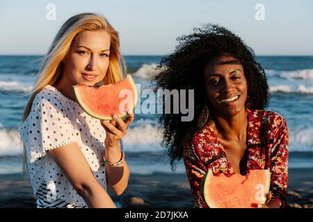 Amis mangeant une tranche de pastèque sur la plage pendant la journée ensoleillée Banque D'Images