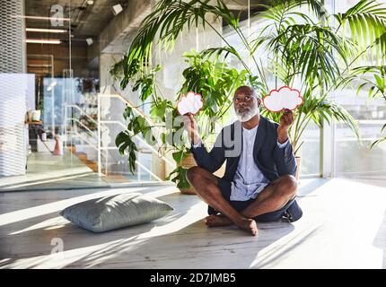 Contemplant un homme tenant une bulle de pensée tout en étant assis avec une jambe croisée à la maison Banque D'Images