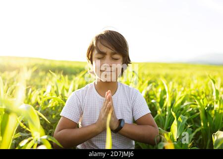 Garçon souriant pratiquant le yoga tout en étant assis sur l'herbe dans la prairie Banque D'Images