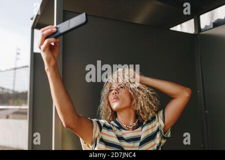 Une femme qui colle à la langue tout en prenant son selfie à travers son smartphone contre les murs métalliques Banque D'Images