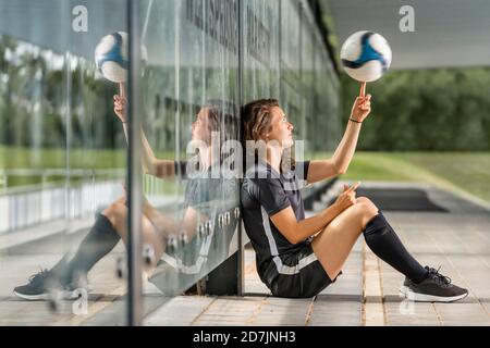 Une joueuse de football fait tourner la balle sur le doigt tout en étant assise paroi en verre Banque D'Images