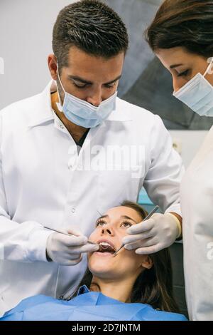 Dentiste masculin dans le masque et les gants examinant les dents de Pretty patient avec l'aide d'une assistante féminine à la clinique Banque D'Images