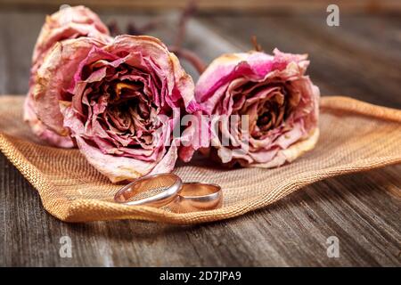 Anneaux de mariage et roses fleurs séchées sur fond de bois. Banque D'Images