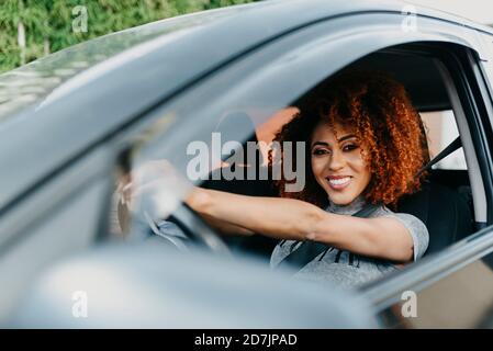 Jeune femme souriante avec une voiture de conduite à cheveux afro vue à travers fenêtre Banque D'Images