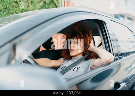 Jeune femme avec la main dans les cheveux en voiture de conduite vu à travers fenêtre Banque D'Images