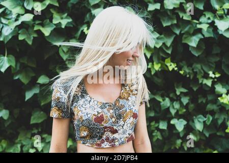 Jeune femme souriante qui se secoue les cheveux tout en se tenant contre les plantes stationnement