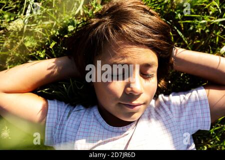 Garçon avec les mains derrière la tête dormant sur l'herbe dans le pré Banque D'Images