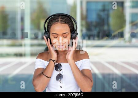 Jeune femme avec casque d'écoute de la musique tout en se tenant contre le verre mur en ville Banque D'Images