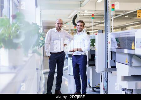 Des hommes souriants tenant la télécommande tout en se tenant debout près des machines en usine Banque D'Images