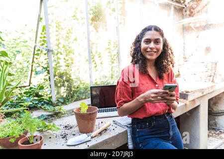 Messagerie texte femme mûre souriante sur smartphone debout dans le hangar de jardin Banque D'Images