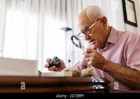 Homme âgé à la retraite utilisant la loupe pour la recherche de fossiles et minéraux à la maison Banque D'Images