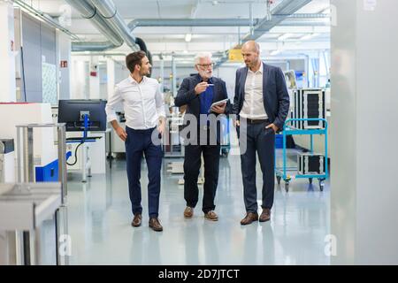 Manager senior avec des collègues discutant sur tablette numérique tout en marchant à l'usine éclairée Banque D'Images