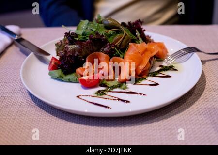 picata de saumon avec câpres et salade fraîche mélangée sur une assiette. Menu du restaurant. Tranches de saumon légèrement salé avec câpres, citron et aneth sur un Banque D'Images