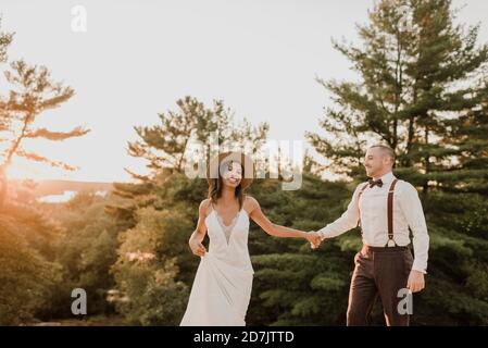 Couple souriant tenant les mains en se tenant debout dans la forêt pendant le coucher du soleil Banque D'Images