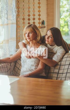 Une fille affectueuse de 20 ans embrasse une mère âgée de derrière, tandis qu'une maman assise sur un canapé les gens posant regardant l'appareil-photo sourire se sent heureux, concept de mu Banque D'Images