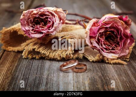 Anneaux de mariage et roses fleurs séchées sur fond de bois. Banque D'Images