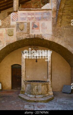 Cour du Palazzo Comunale, hôtel de ville de la cité médiévale, avec une ancienne citerne et des armoiries ornées de fresques, San Gimignano, Toscane, Italie Banque D'Images